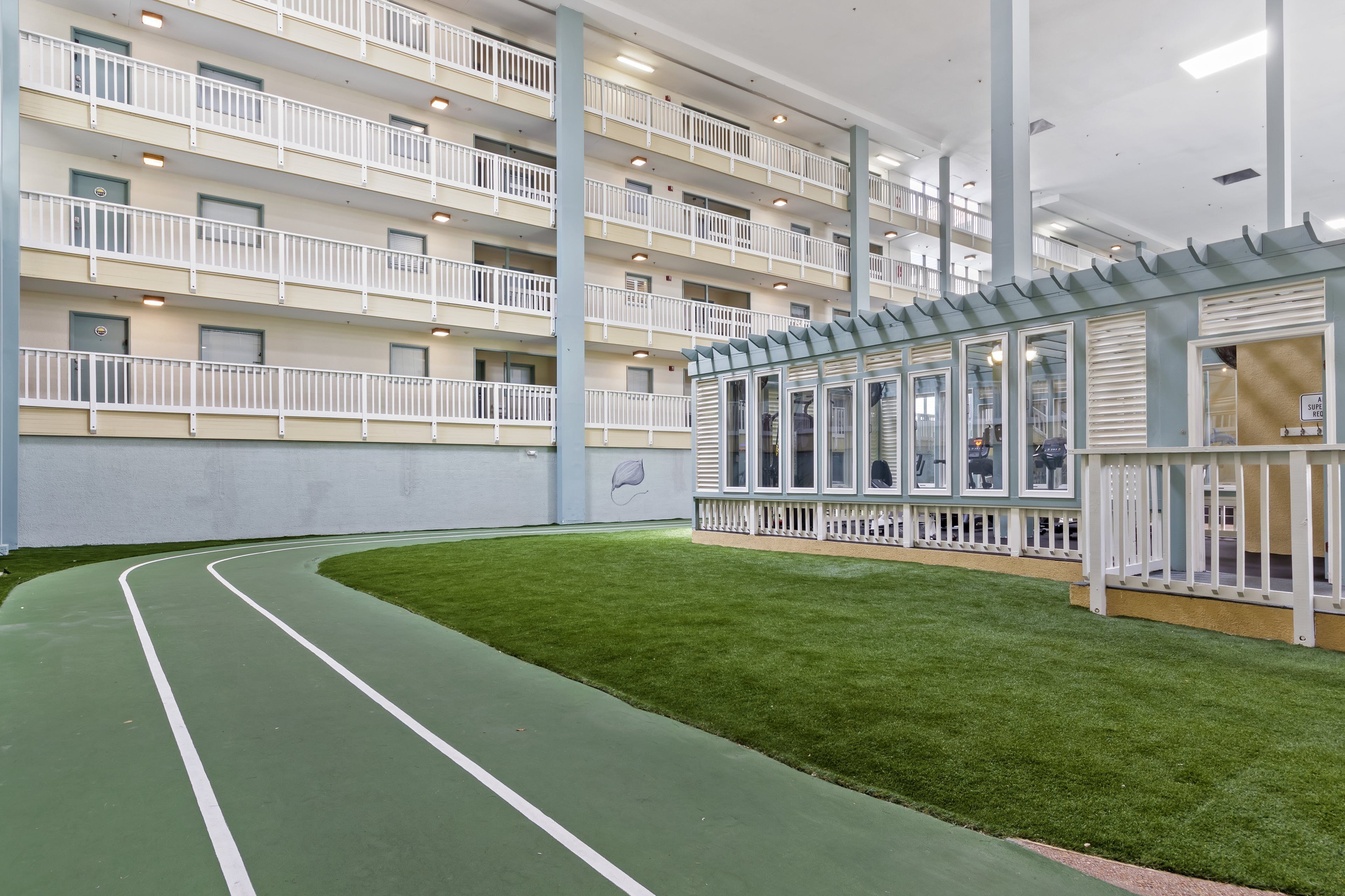 A multi-story building with a green artificial turf track, white railings, and a glass-enclosed area with a view of the interior.