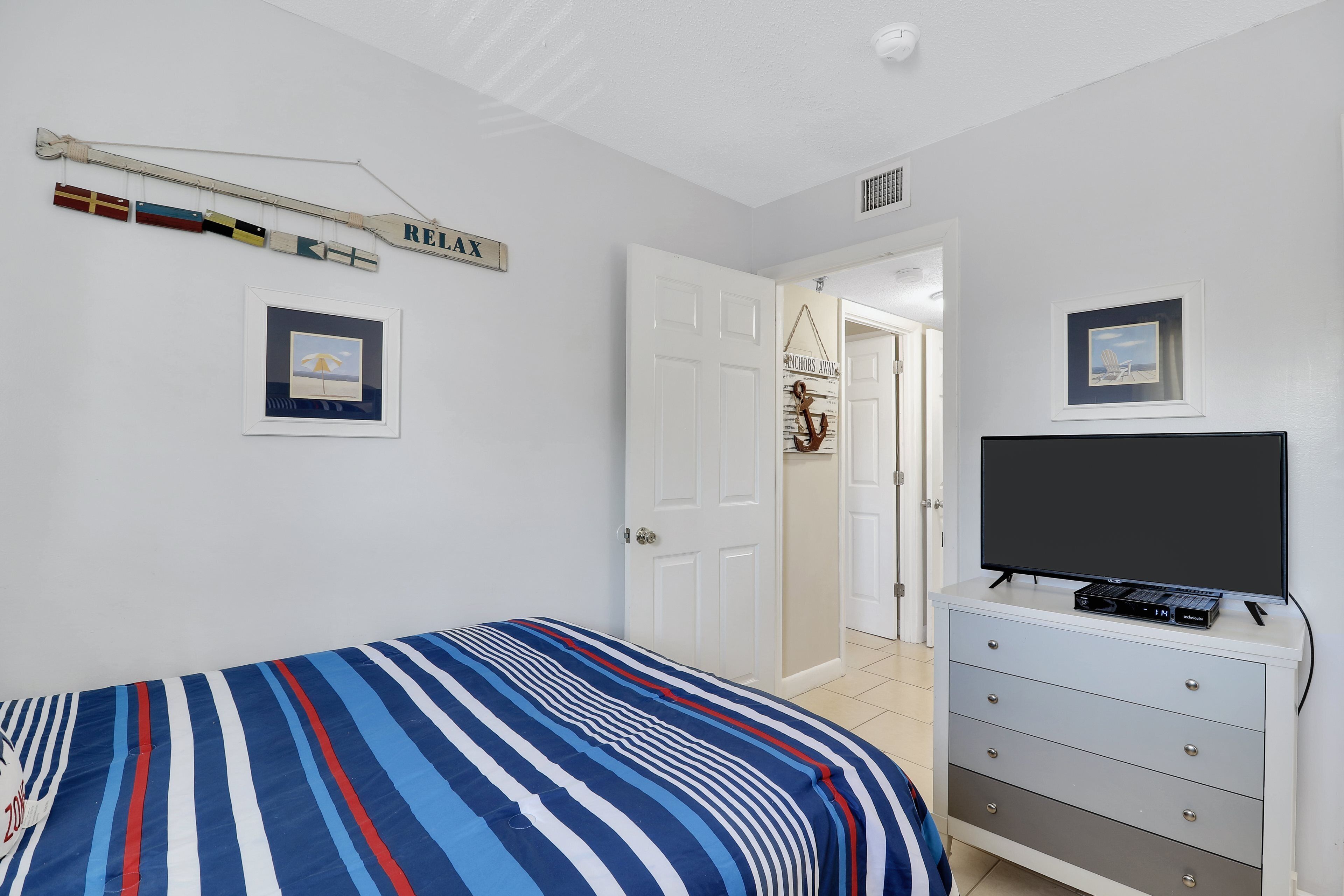 Un dormitorio con una cama, un televisor sobre un aparador y una puerta que conduce a otra habitación.