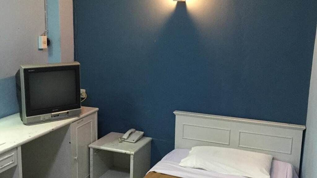 A small room with a bed, a desk with a television, and a bedside table with a phone.