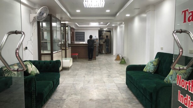 Un hall d'hotel amb sofàs verds, una recepció i una separació de vidre.