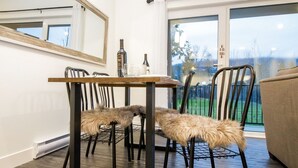 Et spiseområde med et bord og stole, et spejl på væggen og udsigt til det fri gennem store vinduer.