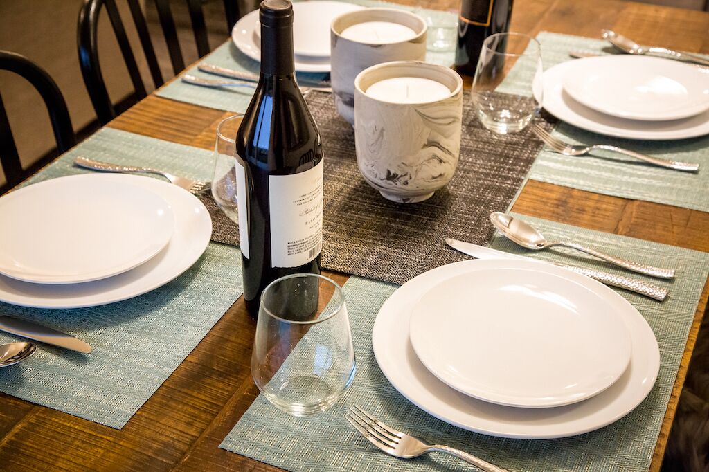 Une table à manger dressée avec de l’assiette blanche, des couverts et une bouteille de vin.