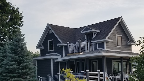 Uma casa de dois andares com varanda grande, deck coberto e jardim bem cuidado.