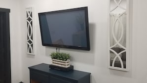 Televisão de tela plana presa à parede acima de um armário de madeira escura, com cortinas decorativas em cada lado.