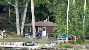 A cabin by a lake with a dock, surrounded by trees. - COZY BEAR LODGE-On UTV/Snowmobile trail, Beachside Cabin w/ Porch, Private dock (St. Germain)