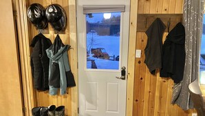 A wooden interior with a door leading to a snowy outdoor scene, a coat rack with jackets, and a pair of boots on the floor. - COZY BEAR LODGE-On UTV/Snowmobile trail, Beachside Cabin w/ Porch, Private dock (St. Germain)