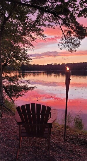 Tuoli ja taskulamppu järven rannalla auringonlaskun aikaan.