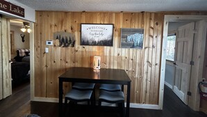 A cabin interior with a wooden wall, a welcome sign, a table with chairs, and a ceiling light. - COZY BEAR LODGE-On UTV/Snowmobile trail, Beachside Cabin w/ Porch, Private dock (St. Germain)