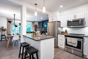 A modern kitchen with white cabinets, stainless steel appliances, and a central island with stools. - Revelation Retreat by Revelstoke Vacations (Revelstoke)