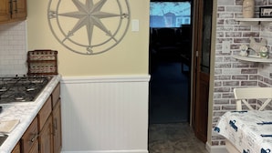 A kitchen with wooden cabinets, a stove, a white countertop, a compass wall decoration, and a brick-patterned wall.