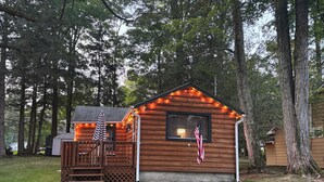 A small wooden cabin with a porch, an American flag, and string lights.