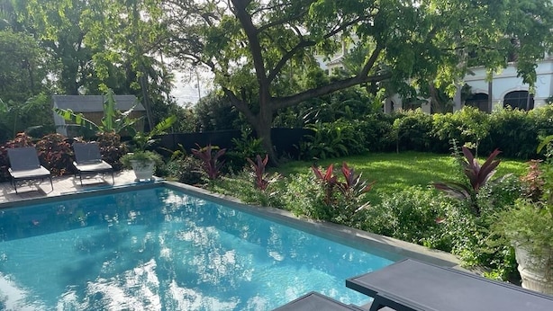 Una piscina con sillones de descanso, rodeada de abundante vegetación y un jardín cuidado.