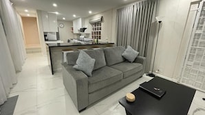 Una sala moderna con un sofá gris, una mesa de centro negra y una cocina al fondo.