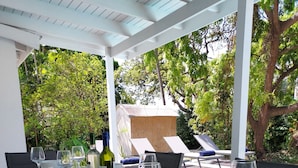 Un área de comedor al aire libre con una mesa de madera dispuesta para una comida, rodeada de sillas y un espacio de estar cubierto.