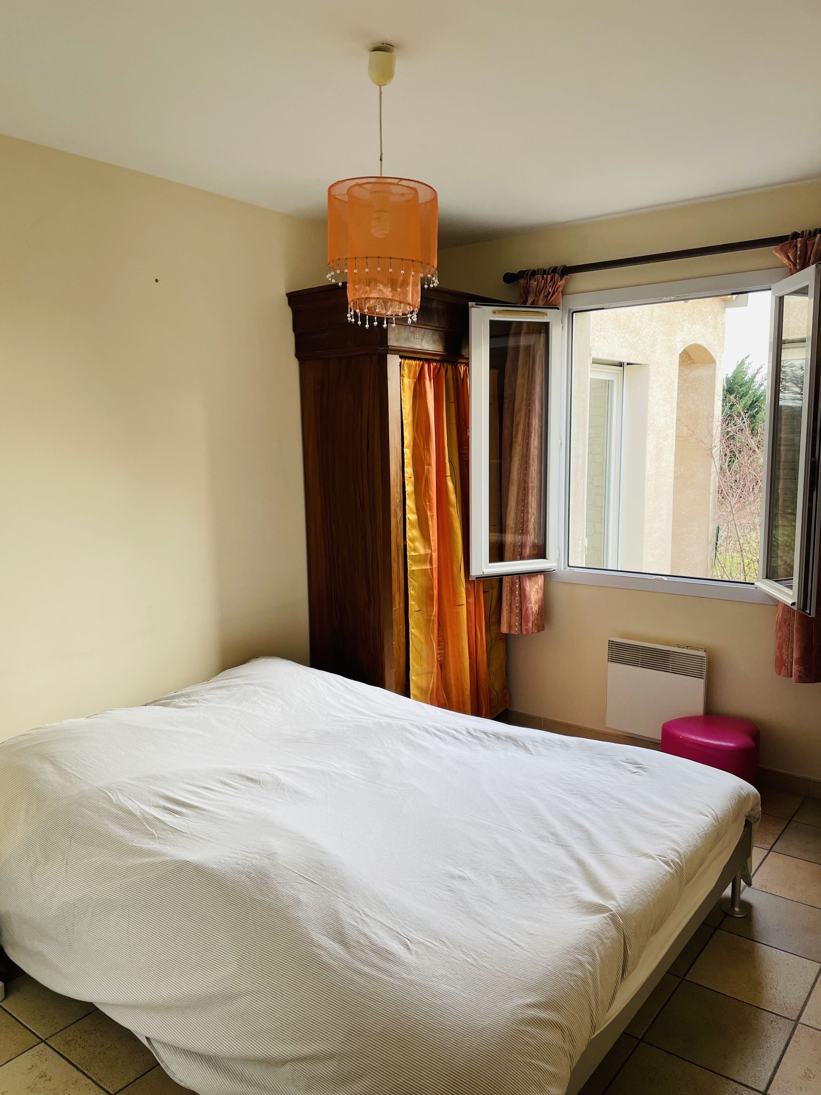 Un dormitorio con cama, ventana con cortinas, radiador y lámpara colgante.