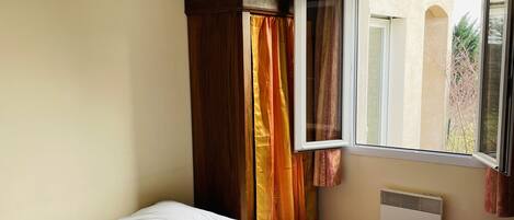 Un dormitorio con cama, ventana con cortinas, radiador y lámpara colgante.
