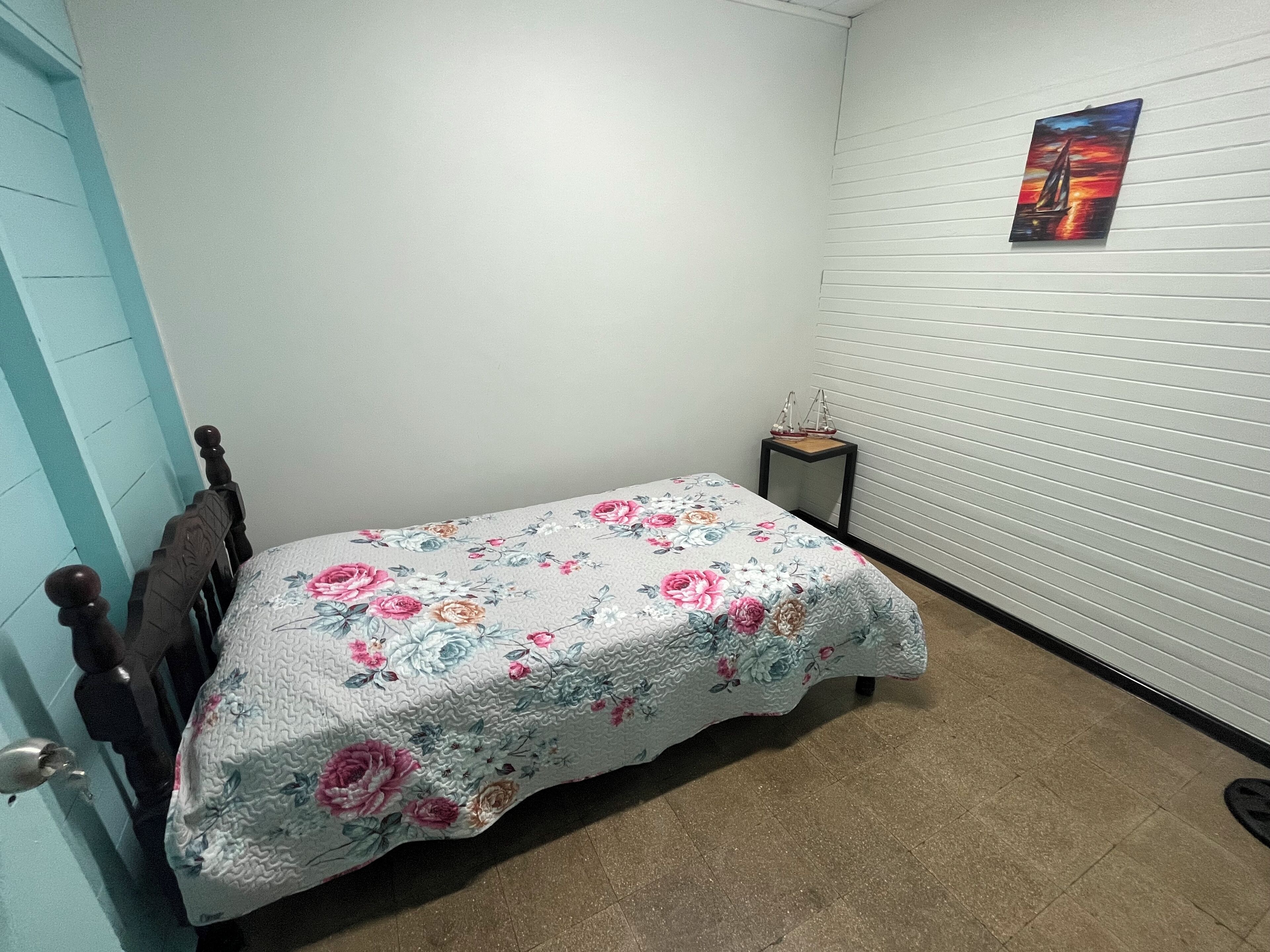 Une petite chambre à coucher, bien rangée, avec un lit, une table de chevet et un tableau accroché au mur.