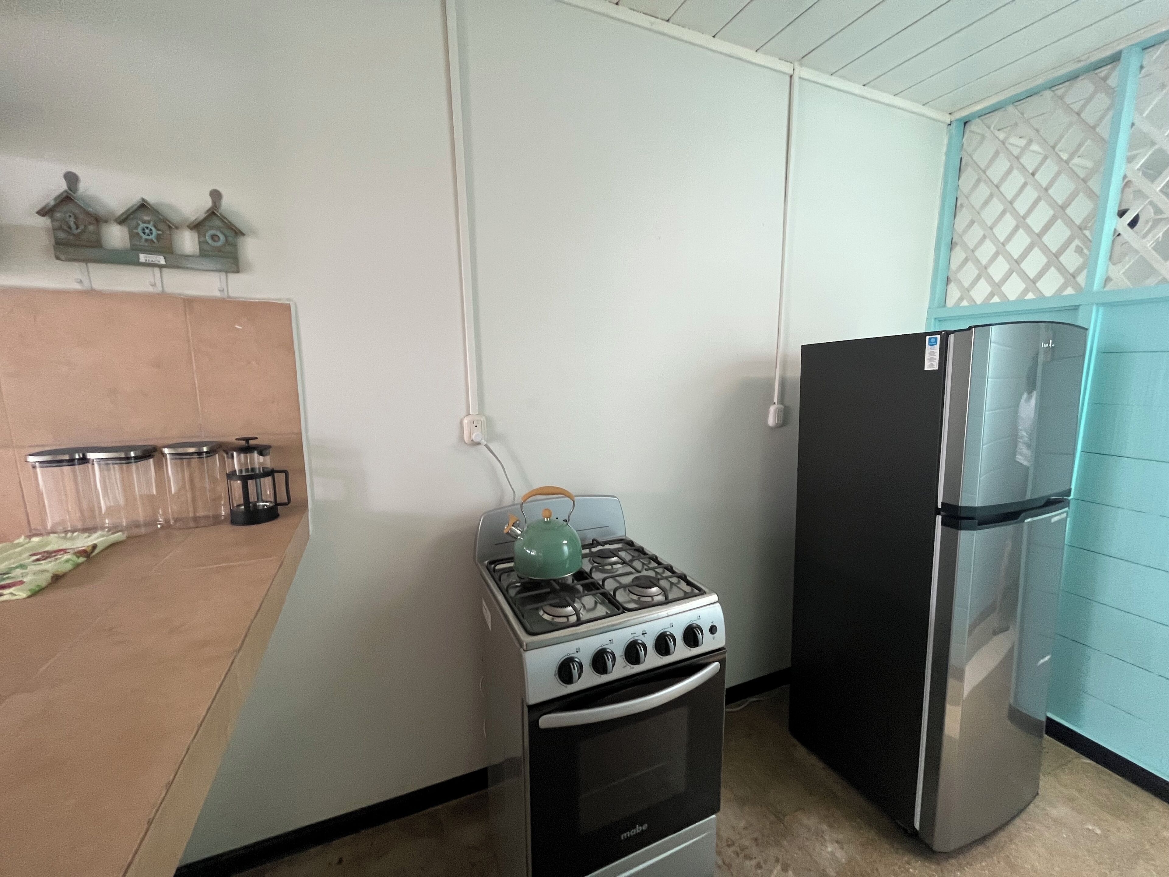 Una cocina con estufa a gas, horno y un refrigerador negro. Hay tres recipientes de vidrio transparente sobre la encimera.