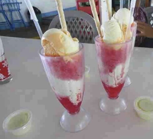 Two glasses of dessert with ice cream and a red topping, possibly a fruit-based drink, on a table.