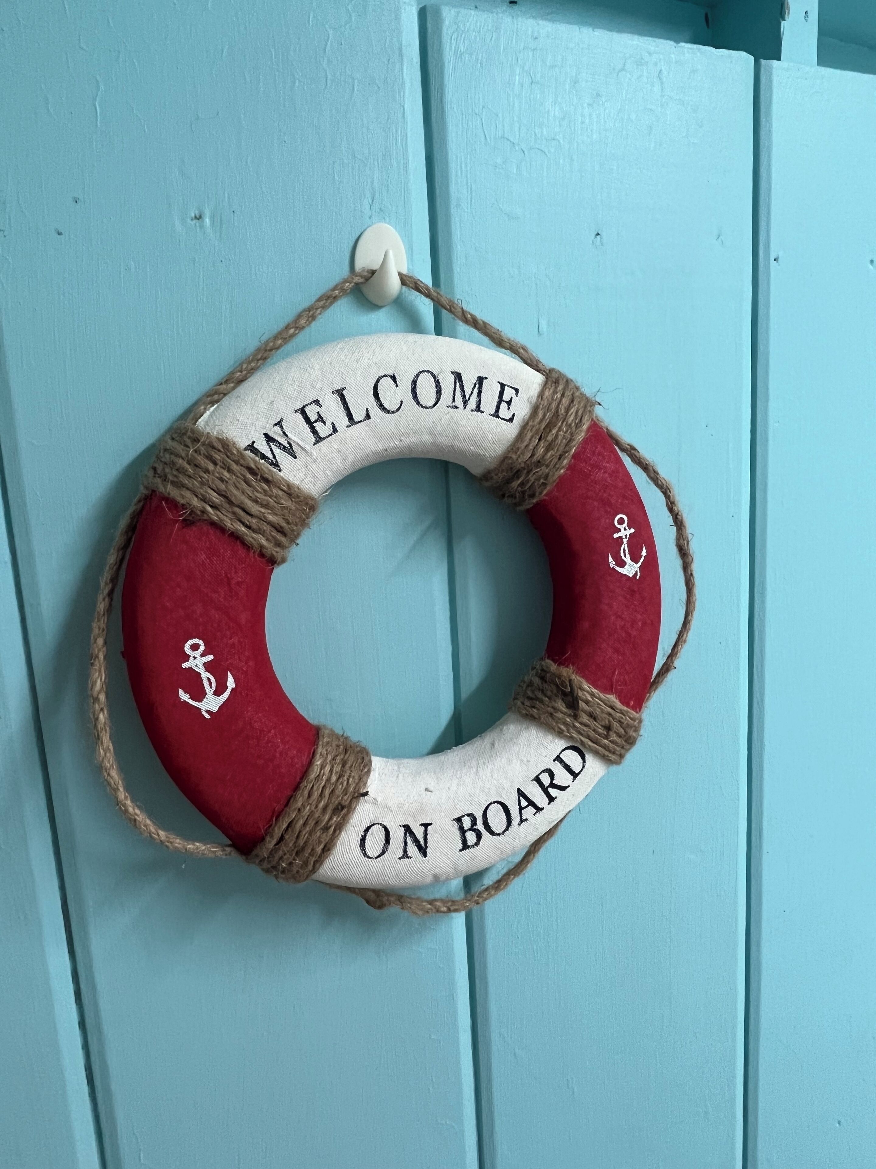 A life preserver with "WELCOME ON BOARD" text and anchor designs, hanging on a light blue door.