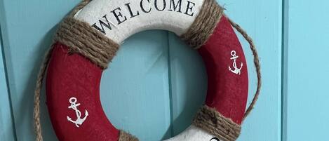 A life preserver with "WELCOME ON BOARD" text and anchor designs, hanging on a light blue door.