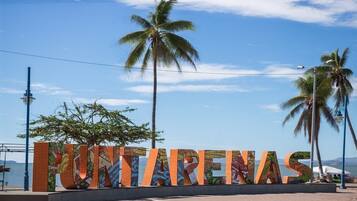 Un letrero con la palabra 'PUNTARENAS' en letras grandes y coloridas, con palmeras y un cielo despejado al fondo.