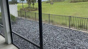 A view of a golf course through a window with a metal railing and gravel ground. - Stunning Golf Front 3 BR Villa in The Villages (THE VILLAGES)