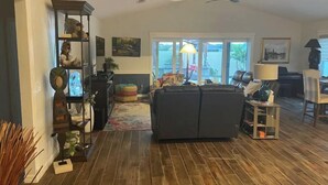 A spacious living room with a dark-colored sofa, a wooden floor, and a ceiling fan. - Stunning Golf Front 3 BR Villa in The Villages (THE VILLAGES)