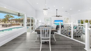 A spacious dining area with a pool view, white railings, and modern lighting fixtures. -  Luxury WaterFront Home, Putting Green, Bocce, Pool/PPong Tbl (Marco Island)