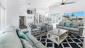 A spacious living room with a grey sofa, patterned armchairs, a coffee table, and a ceiling fan. -  Luxury WaterFront Home, Putting Green, Bocce, Pool/PPong Tbl (Marco Island)