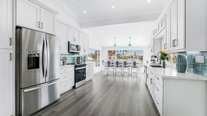 A modern kitchen with white cabinetry, stainless steel appliances, and a central island with seating. -  Luxury WaterFront Home, Putting Green, Bocce, Pool/PPong Tbl (Marco Island)