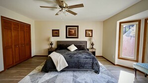 A bedroom with a bed, two bedside tables with lamps, a ceiling fan, a large window, and a wooden wardrobe. - The Akes house is a great place to relax and let all your aches fade away.  (Cheyenne)