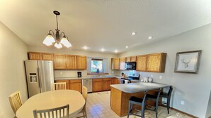 A modern kitchen with wooden cabinets, a stainless steel refrigerator, a built-in oven, and a dining area with a round table and chairs. - The Akes house is a great place to relax and let all your aches fade away.  (Cheyenne)
