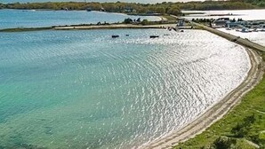 Una casa grande de dos pisos con una escalera principal destacada, rodeada de exuberante vegetación y un camino curvo que conduce a una playa arenosa.