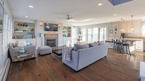 Amplia sala de estar con chimenea, sofá, mesa de centro y una zona de cocina con taburetes de bar.