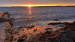 Una puesta de sol costera con un litoral rocoso y mar tranquilo.