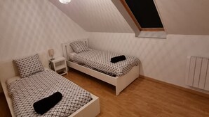 Une chambre avec un plafond en pente, un puits de lumière, deux lits avec une literie à motifs géométriques, une table de chevet avec une lampe et un radiateur.