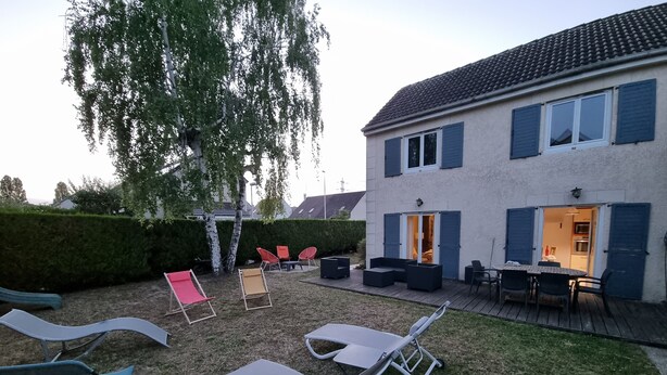 Un jardin avec des meubles d’extérieur, une pergola et une maison aux volets bleus.