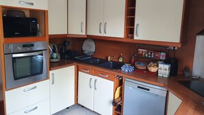 Une cuisine de taille réduite, avec des meubles blancs, un four à micro-ondes, un four traditionnel, un évier et un lave-vaisselle.