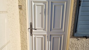 Une porte blanche surmontée d’une fenêtre en demi-lune, un paillasson sur lequel on peut lire : « Ici, c’est mon havre de paix », et une petite marche menant à la porte.