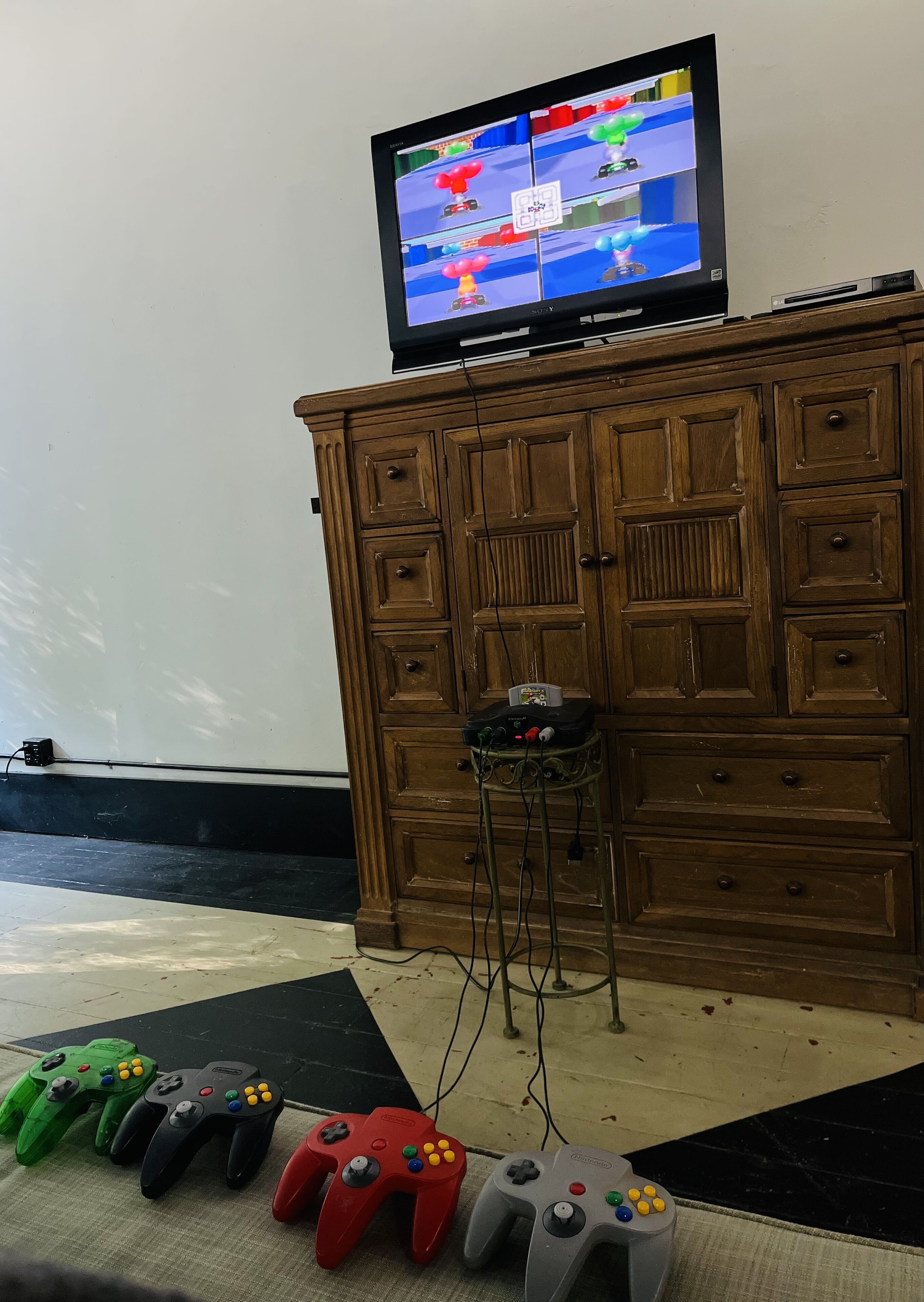 A wooden cabinet with a television on top, a small stool, and several game controllers on the floor.