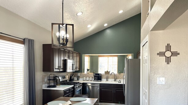 A modern kitchen with dark cabinets, stainless steel appliances, and a dining area with a wooden table and placemats. - ABQ Home Overlooking Mountain- Near Sandia Tramway + Balloon Fiesta  (Albuquerque)