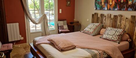 A bedroom with a large bed, a wooden headboard, a window with curtains, a radiator, and a painting on the wall.