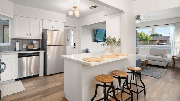 Una cucina moderna con mobili bianchi, un frigorifero in acciaio inossidabile, un'isola integrata con sgabelli e una TV a schermo piatto montata a parete.