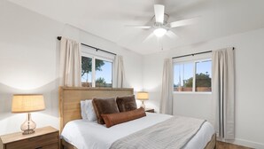 Una camera da letto con un letto di legno, due comodini con lampade, una ventola a soffitto e finestre con tende.