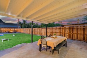 Une terrasse extérieure avec une table et des chaises, un foyer et une vue sur une montagne et un lac au crépuscule.