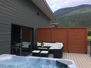 Um terraço com hidromassagem, área de estar externa e vista para uma montanha arborizada.