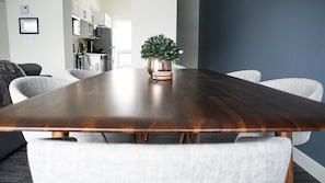 Uma sala de conferência com uma mesa de madeira comprida, cadeiras brancas e um vaso de planta.