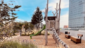 A playground with a slide, wooden benches, and a rope barrier. - Sunrise over the park (Prater) and roof terrace pool (Wien)