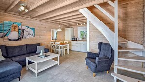 Ein geräumiger Wohnbereich mit einem dunkelgrauen Sofa, einem weißen Couchtisch und einem grauen Sessel. Eine Holztreppe mit weißer Geländer führt auf eine obere Ebene.